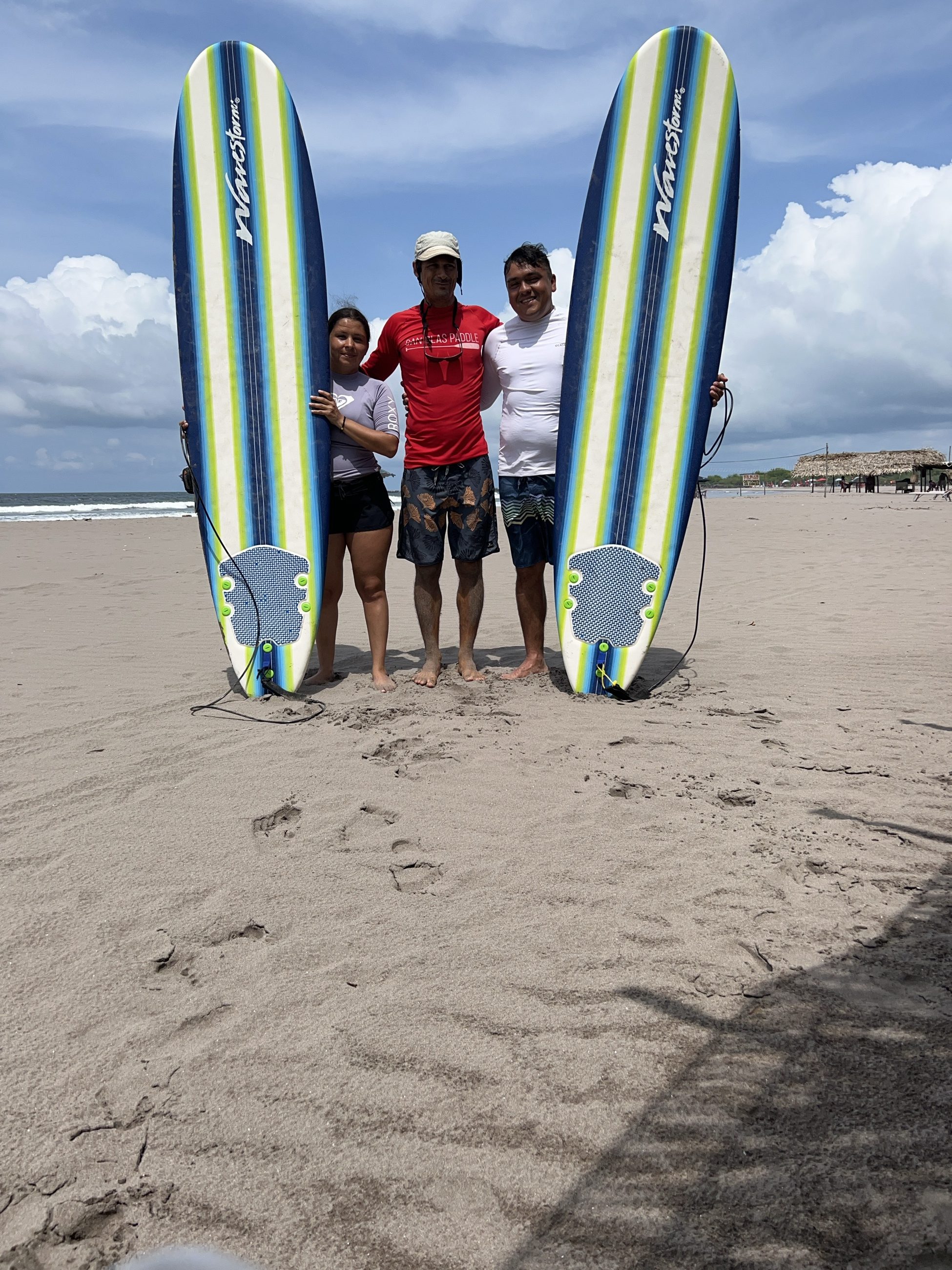 Instructor y dos alumnos en la playa sujetando sus tablas antes de entrar al agua